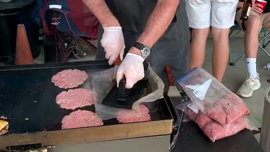 Gloved hands pressing smash burger patties on the Blackstone griddle beside finished cheeseburgers