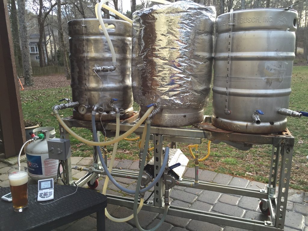 Three-keg all-grain brewing rig on the patio next to a poured glass of beer