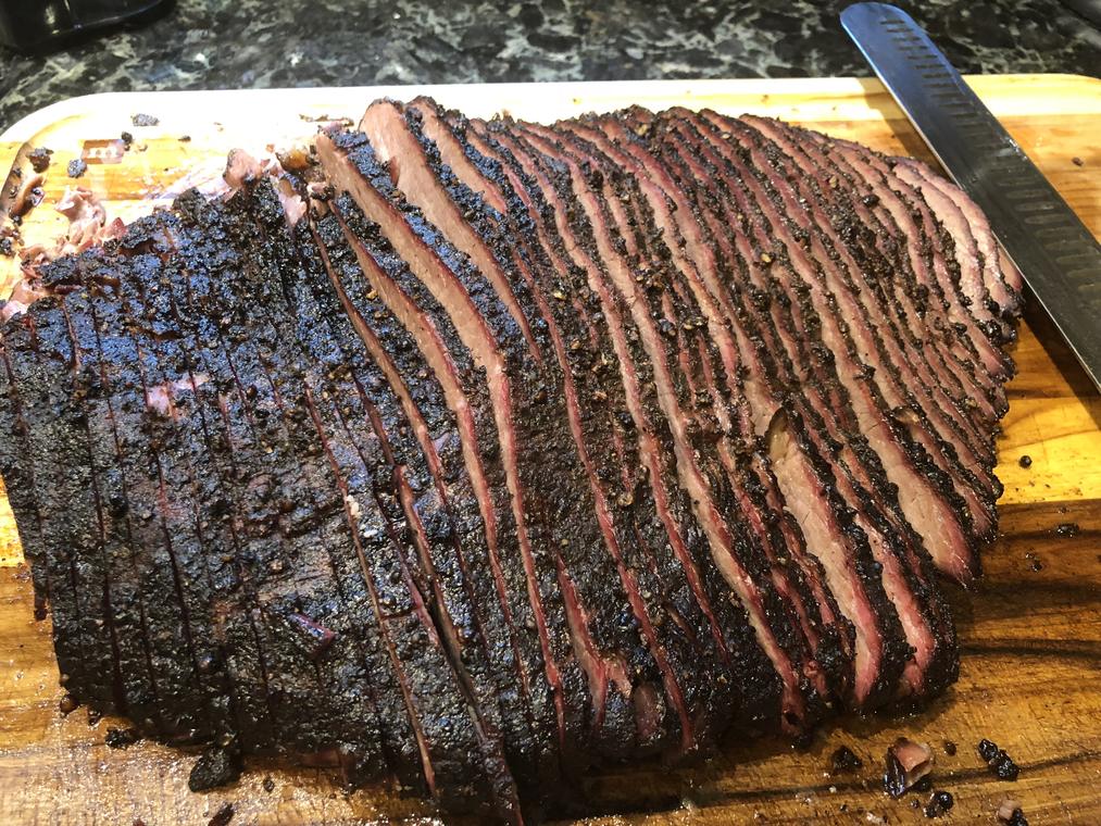 Sliced brisket fanned across a board, smoke ring showing through the bark