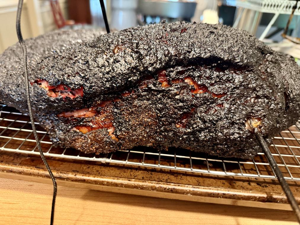A whole packer brisket with black bark, resting on a board