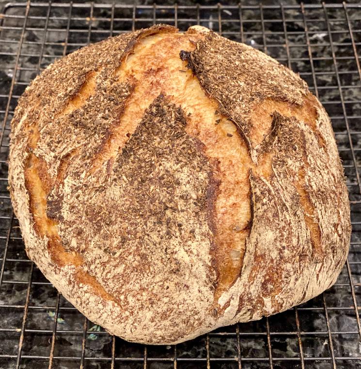 A scored sourdough boule on a cooling rack