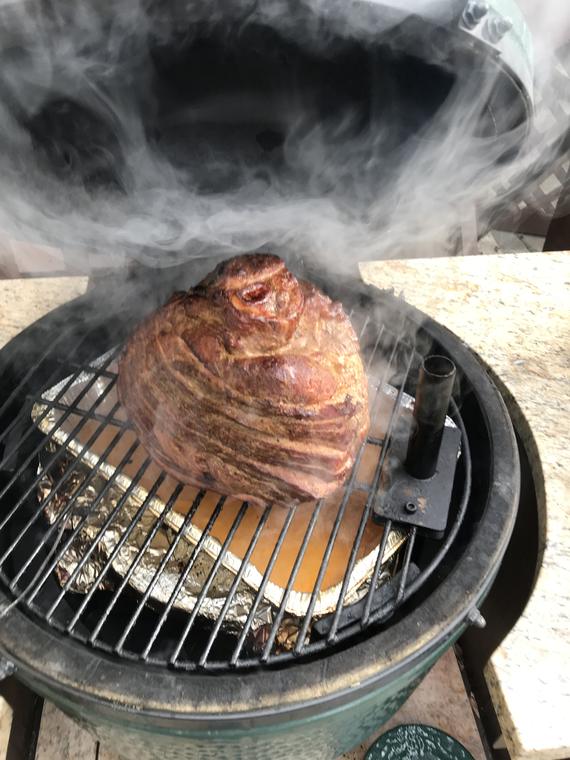 Smoke pouring out of the Big Green Egg around a pork shoulder