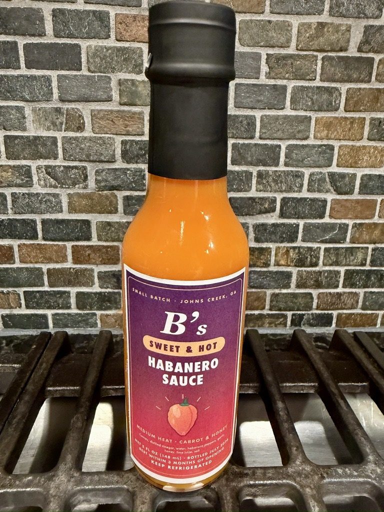 A bottle of B's Sweet and Hot Habanero Sauce on the grill grate